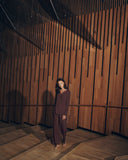 Woman wearing vivid brown Lilith Pajama Set standing in a room with wooden paneling.