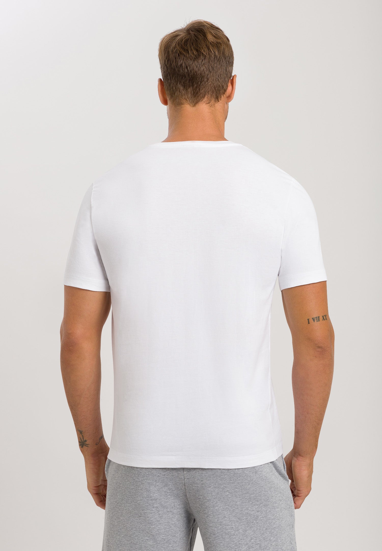 Man wearing a plain white t-shirt and gray pants on a light gray background