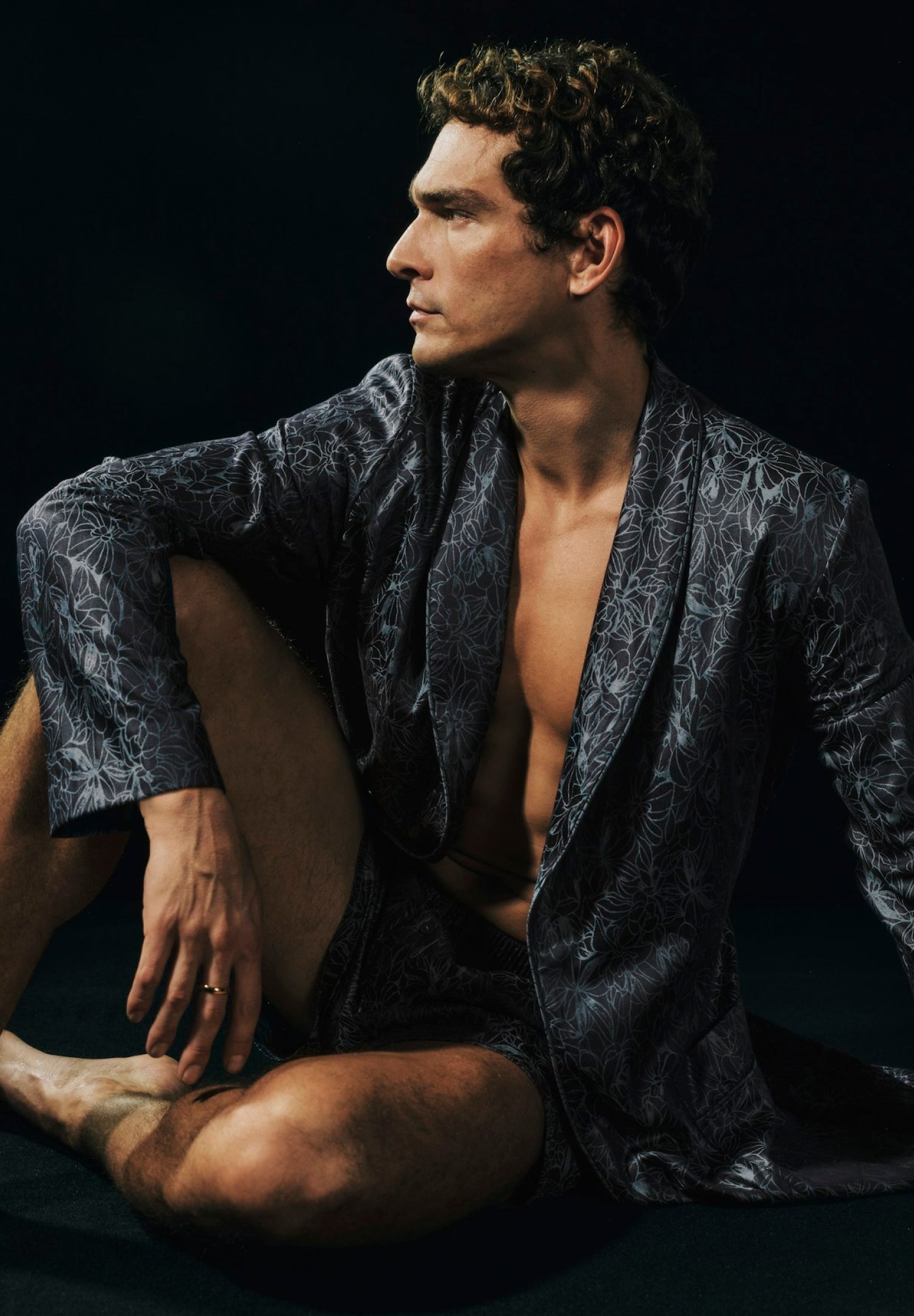 Man wearing a dark patterned robe against a black background