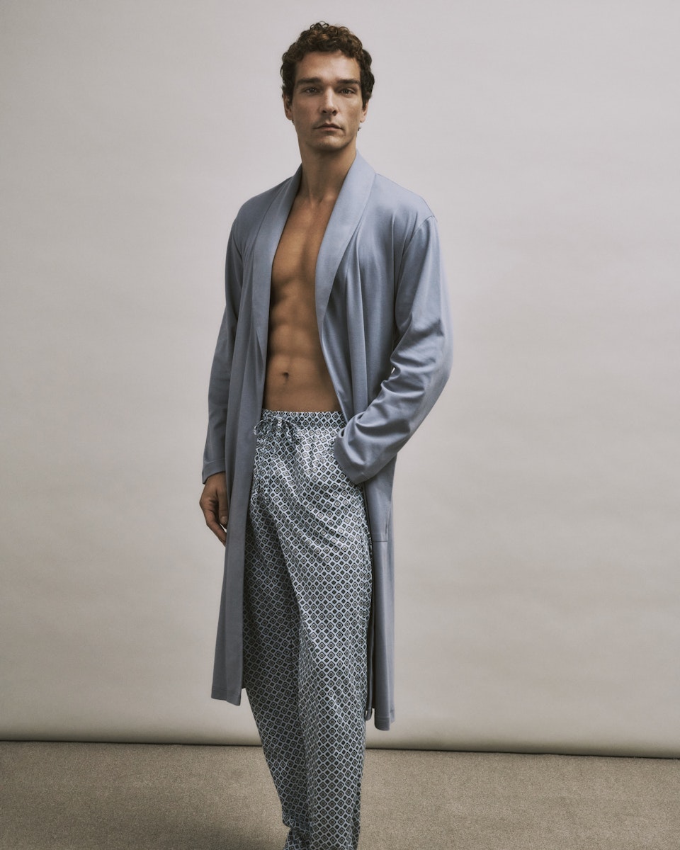Man wearing a light blue robe over patterned pants on a neutral background