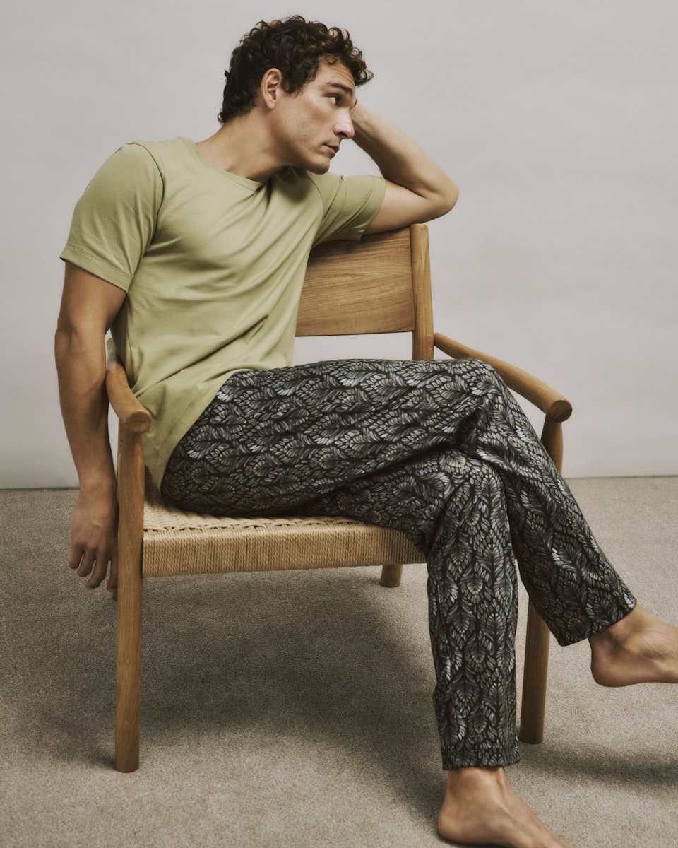 Man sitting on a chair wearing a cardamom shirt and patterned pants.