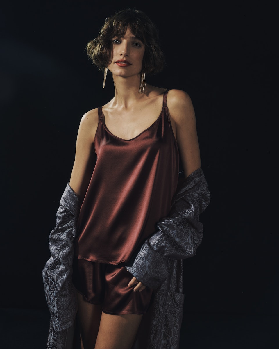 Woman wearing a burgundy satin shorts set with a dark background