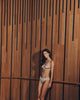 Woman in Lilith lingerie in coffee quartz color standing against a wooden wall with vertical slats