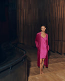 Woman wearing Lilith pink dress and Favourites robe standing in a dimly lit room with wooden walls.