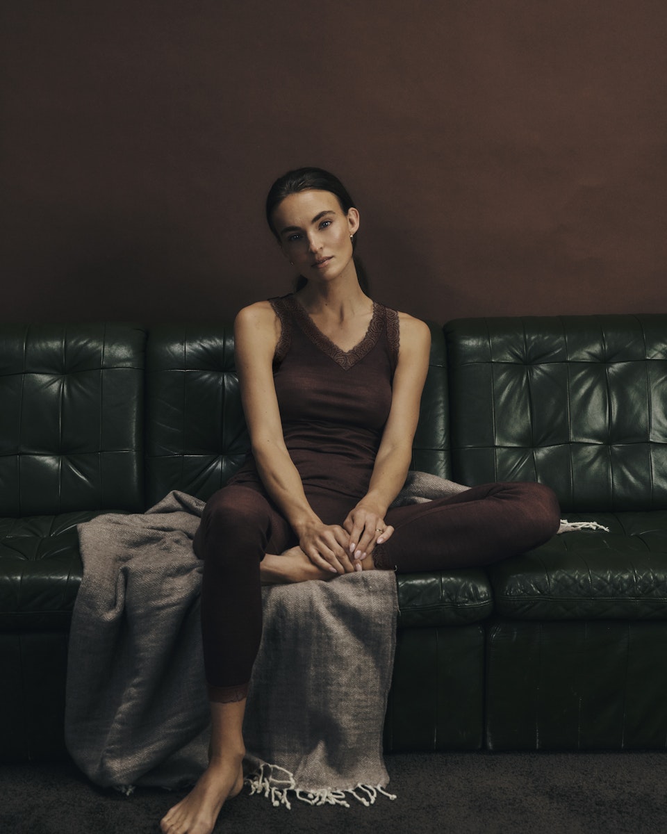 Woman sitting on a dark green leather couch in woolen lace with a plain background