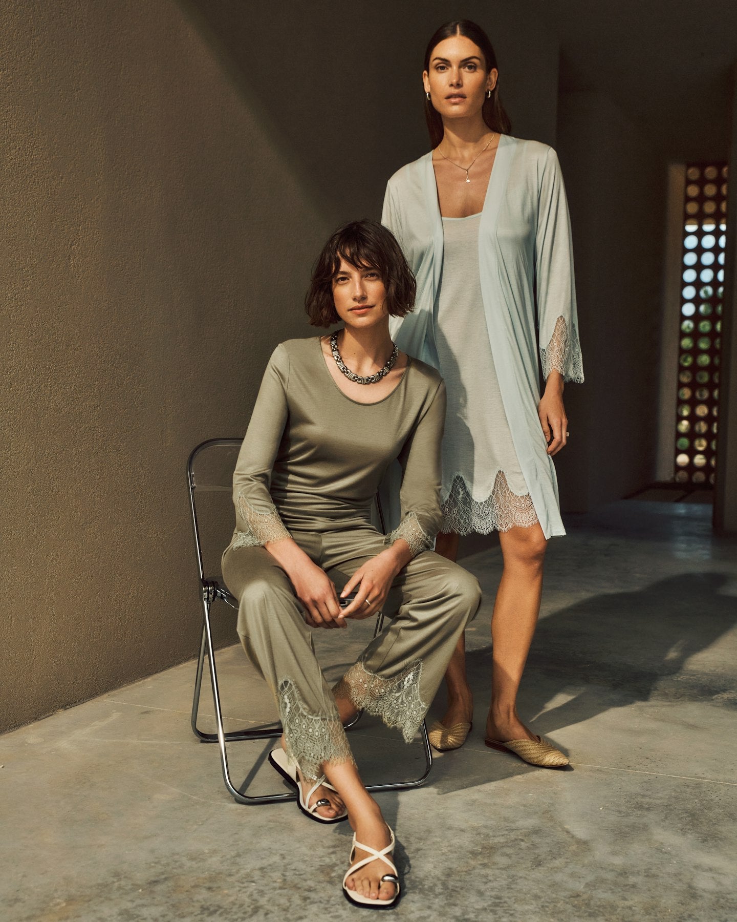 Two women posing together. Women on left is sitting down wearing Melia Pajama Set in Crystal Green.  Women on the right is standing slightly behind wearing Melia Spaghetti Chemise under Melia Robe in Ice Flow.
