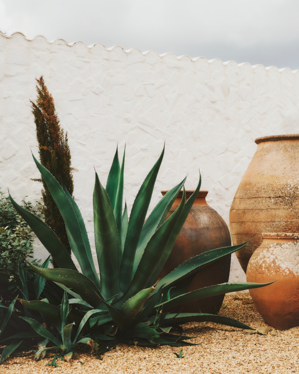 Pants and Large rusted pots placed in front of white stone wall