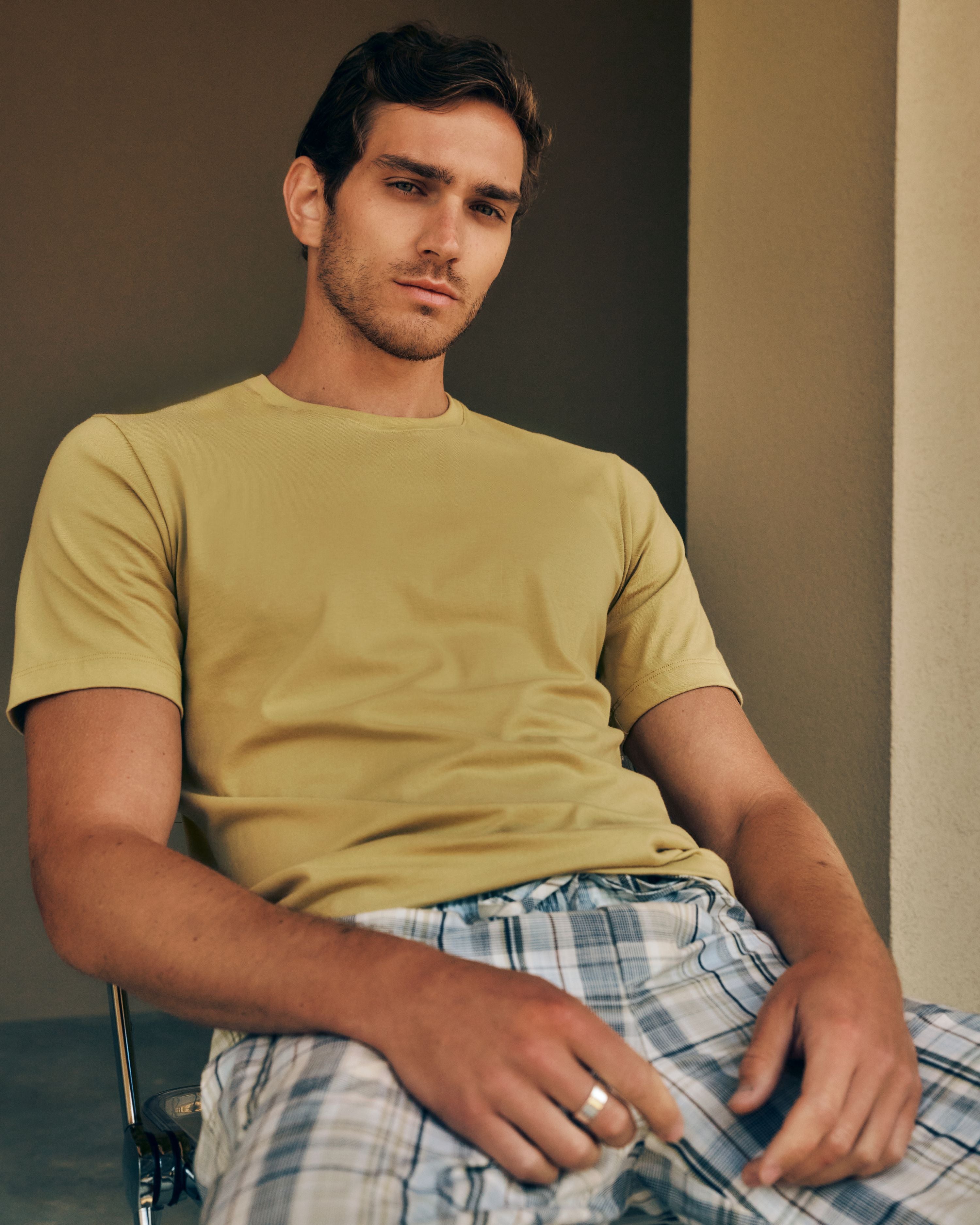 Man relaxing in a chair while wearing Living Shirts in Straw, paired with Night and Day Woven Pants in Gentle Check.