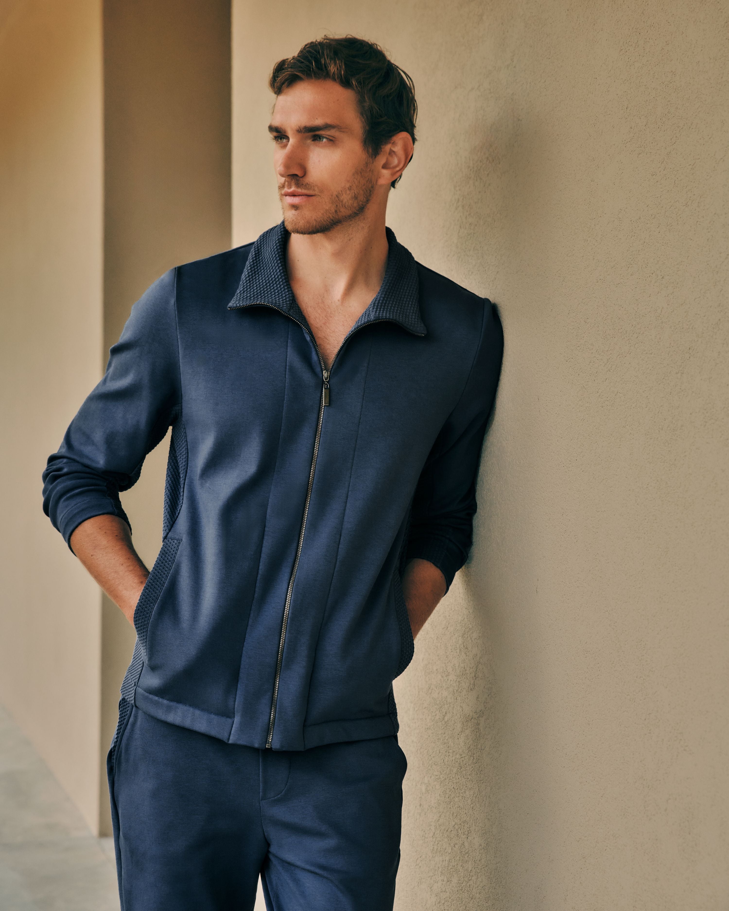 Man leaning against wall wearing Smartwear jacket and pants