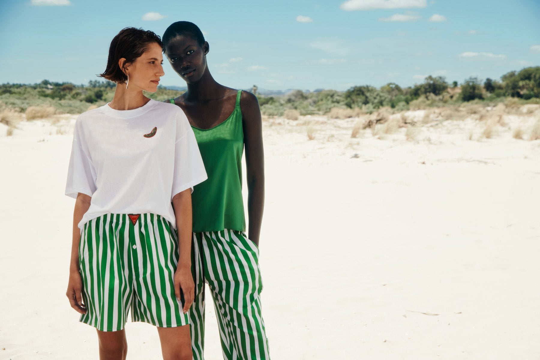 Two women standing in a desert landscape wearing green and white outfits.
