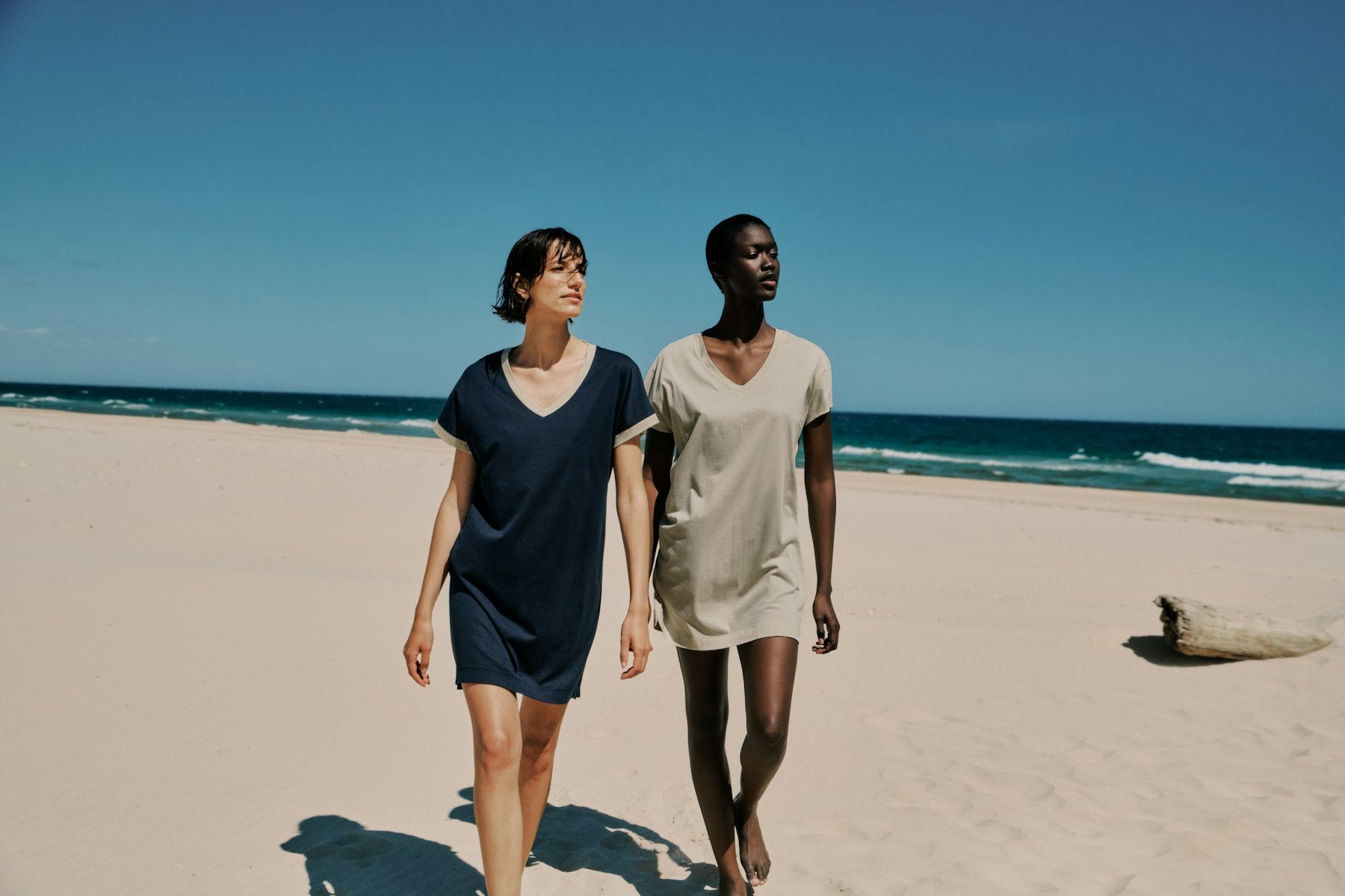 Two people walking on a sandy beach with ocean in the background