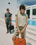 Woman holding an orange handbag with a man in the background by a pool.