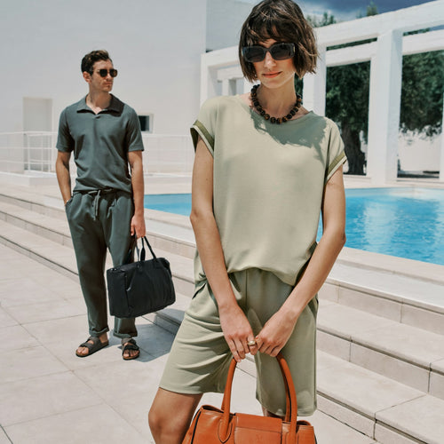 Woman holding an orange handbag with a man in the background by a pool.