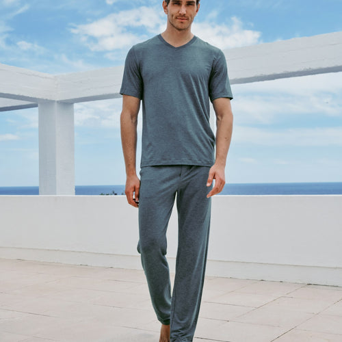 Man wearing a blue pajama set on a rooftop with a blue sky and ocean view.