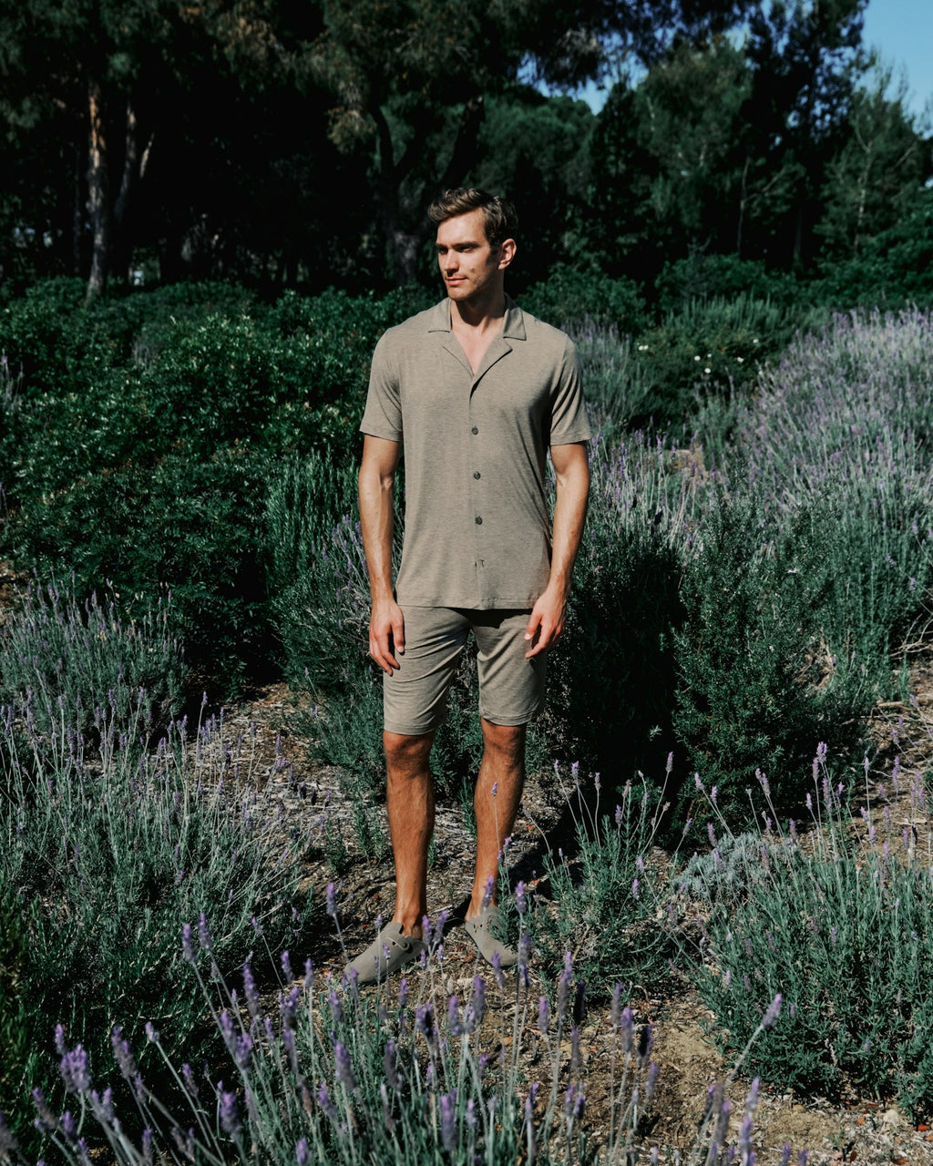 Man standing in a lavender field wearing a brown outfit.