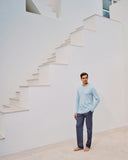 Man wearing a light blue long sleeved top and patterned pants standing in front of a white staircase.