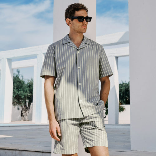 Man wearing a striped shirt and shorts standing in front of white columns with a blue sky.