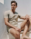 Man sitting on a staircase wearing a beige t-shirt and shorts.