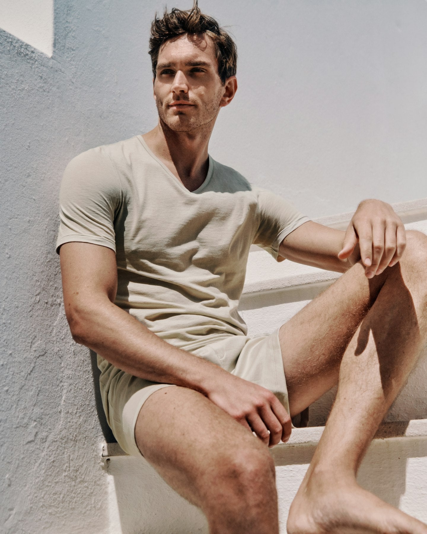 Man sitting on a staircase wearing a beige t-shirt and shorts.