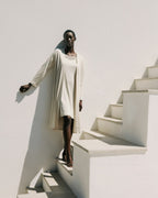 Woman in a long beige coat standing on a white staircase against a white wall