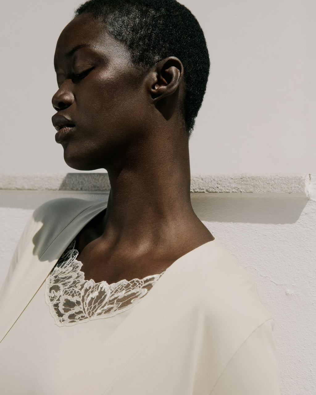 Woman wearing a beige garment with lace detailing against a neutral background