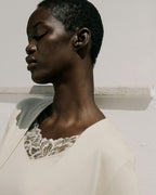 Woman wearing a beige garment with lace detailing against a neutral background