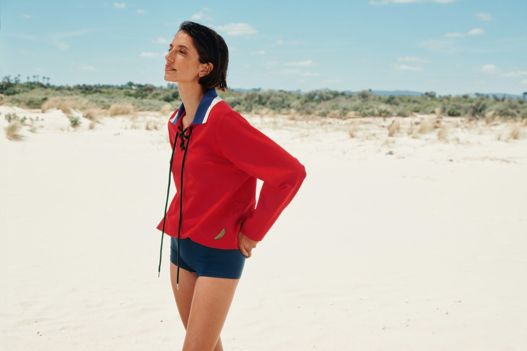 Woman in a red shirt and blue shorts standing on a sandy landscape with a clear sky.