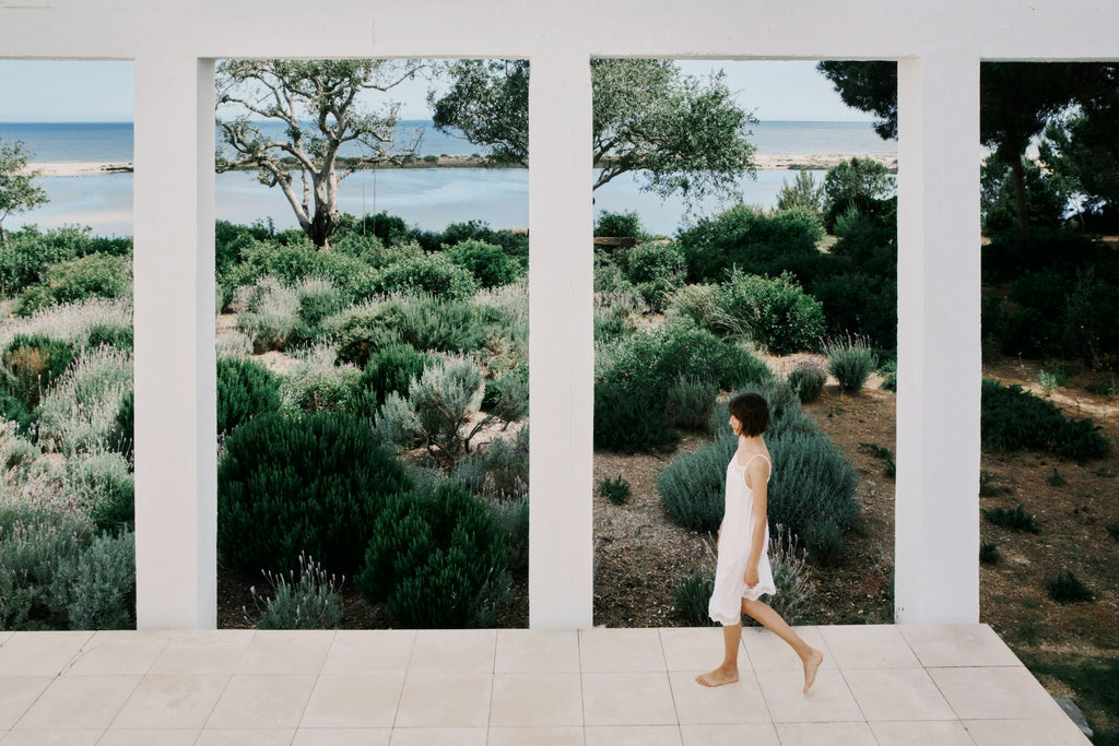 Woman walking on a path with a scenic view of trees and water through large windows.