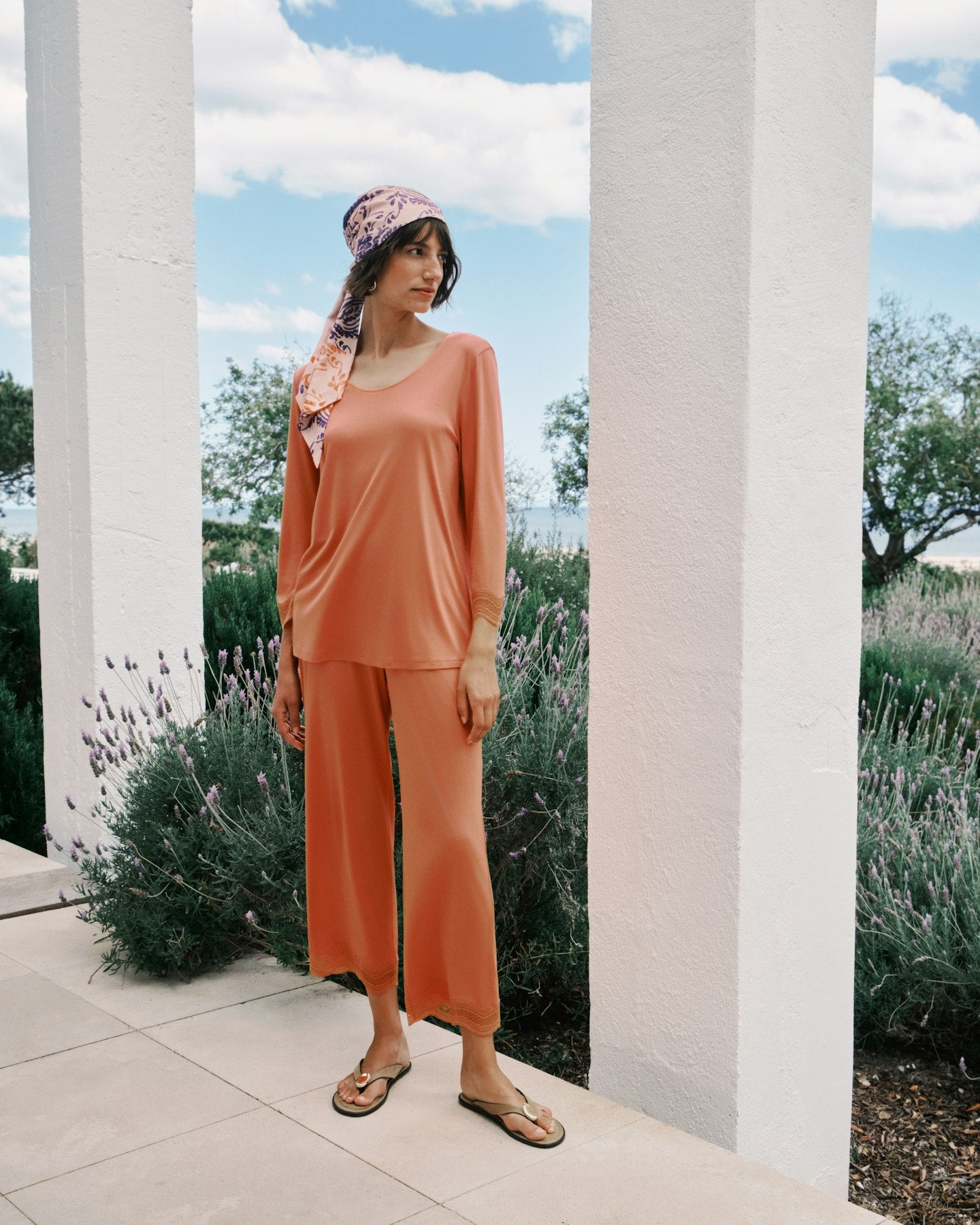 Woman in an orange outfit standing outdoors with columns and lavender in the background