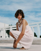 Woman in a light pink dress sitting outdoors with a blue sky background