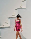 Woman in a pink short pajama set standing on white steps with a white wall background