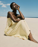 Woman in a yellow dress sitting on a sandy beach with a clear blue sky.