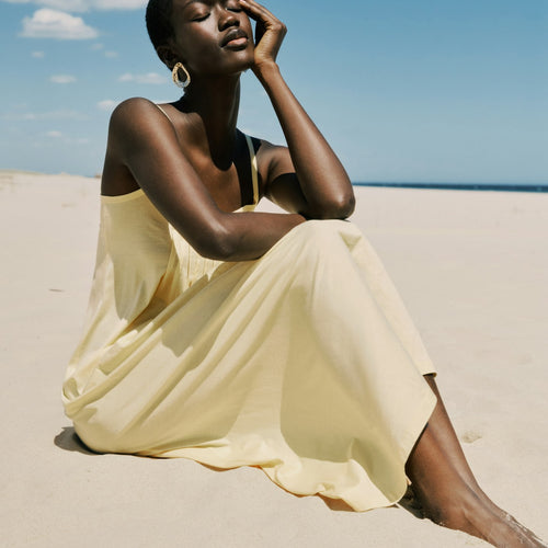 Woman in a yellow dress sitting on a sandy beach with a clear blue sky.