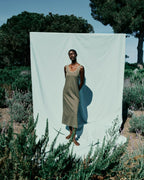 Person standing in a natural setting with a large white sheet draped behind them.