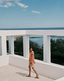 Woman standing on a balcony with a scenic view of trees and water.