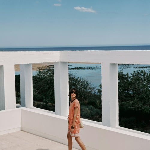 Woman standing on a balcony with a scenic view of trees and water.