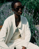 Person wearing sunglasses and a white outfit sitting among lavender plants