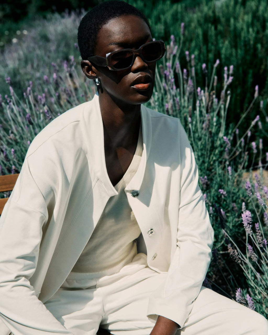 Person wearing sunglasses and a white outfit sitting among lavender plants