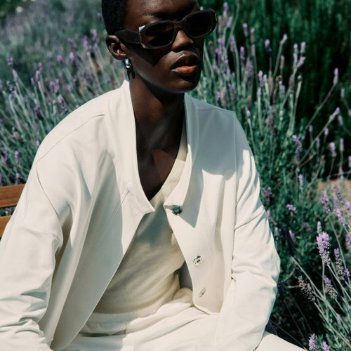 Person wearing sunglasses and a white outfit sitting among lavender plants