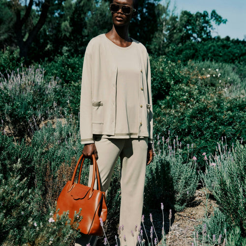 Woman holding an orange handbag in a garden setting