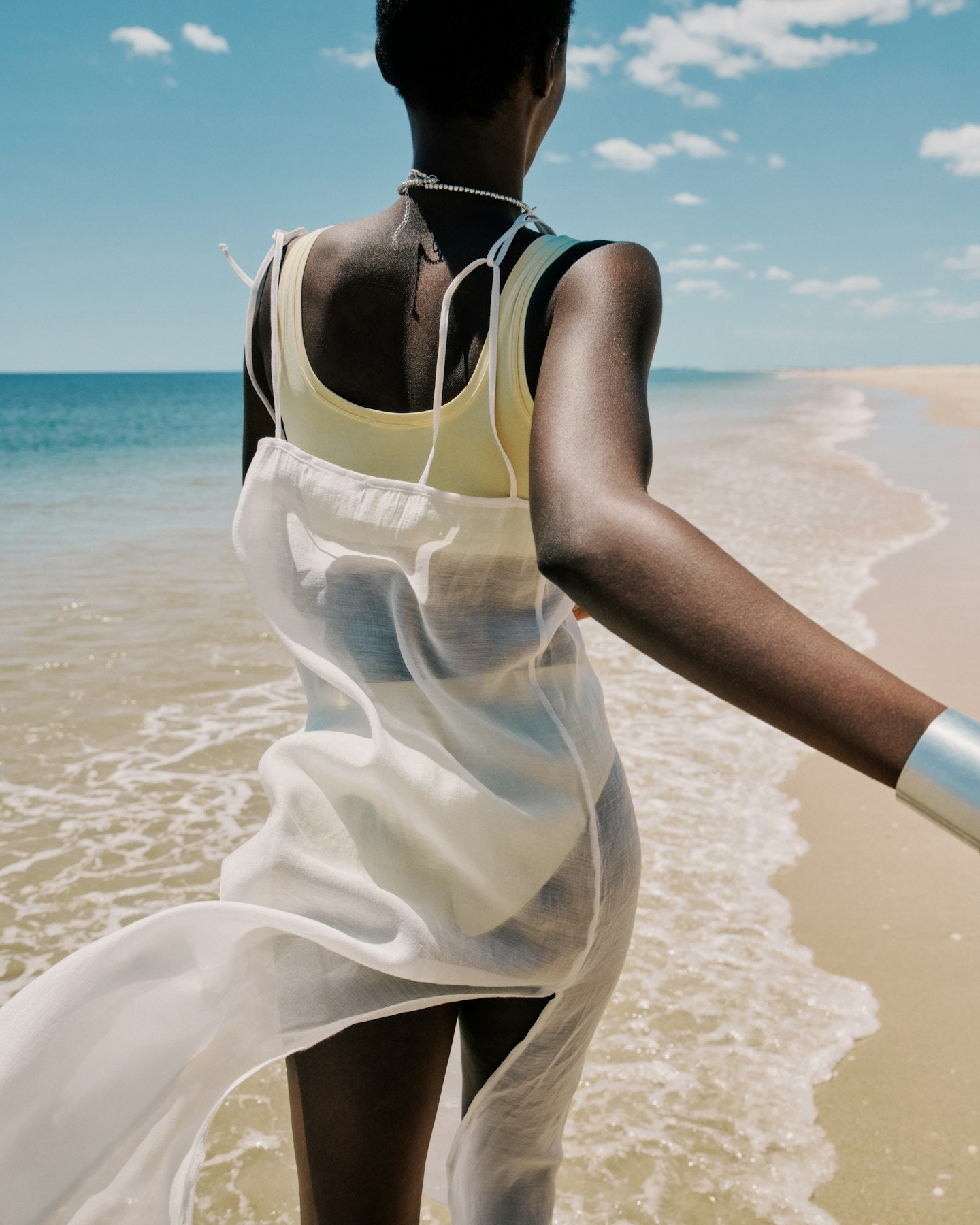 Person in a white dress standing on a beach with ocean and sky in the background