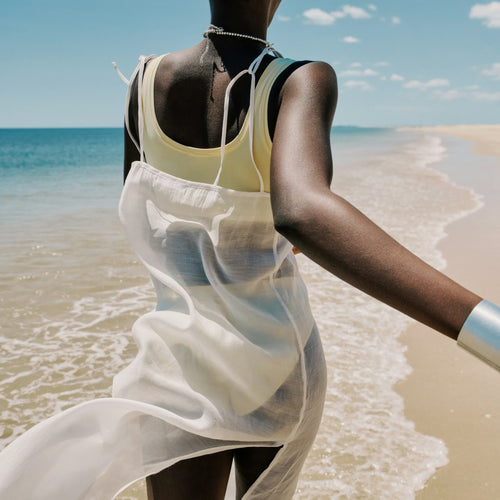 Person in a white dress standing on a beach with ocean and sky in the background