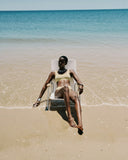 Woman sitting in a chair on a beach with clear blue water and sand.