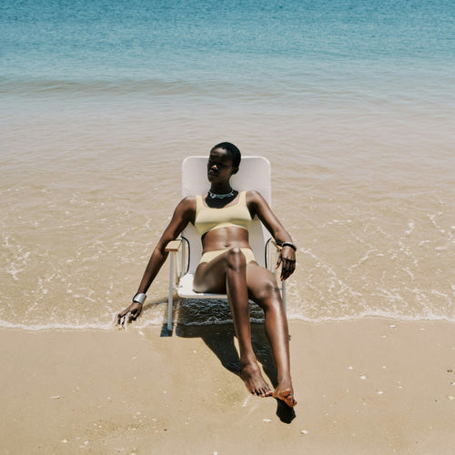 Woman sitting in a chair on a beach with clear blue water and sand.