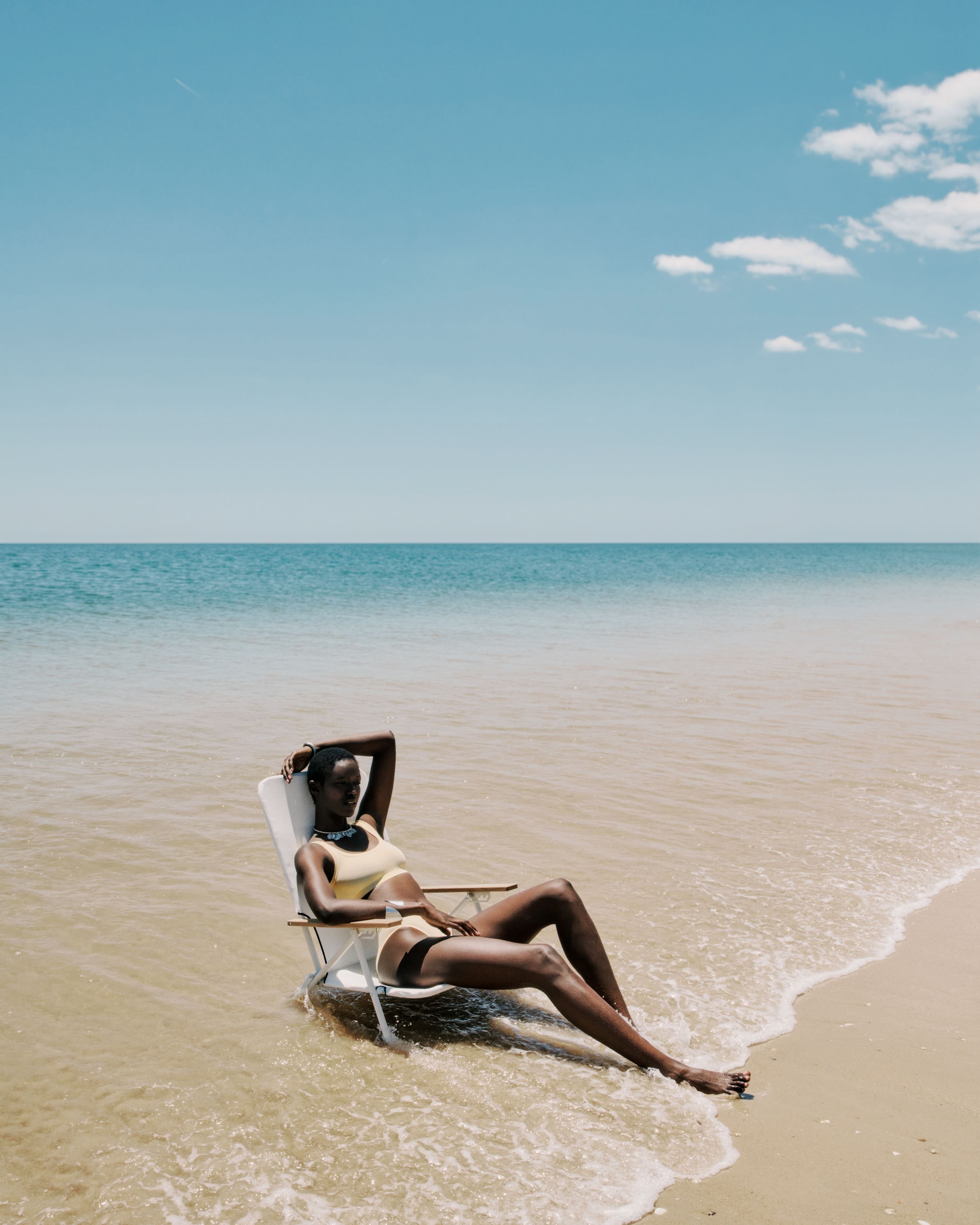 Woman relaxing on a beach chair in shallow water under a clear blue sky.
