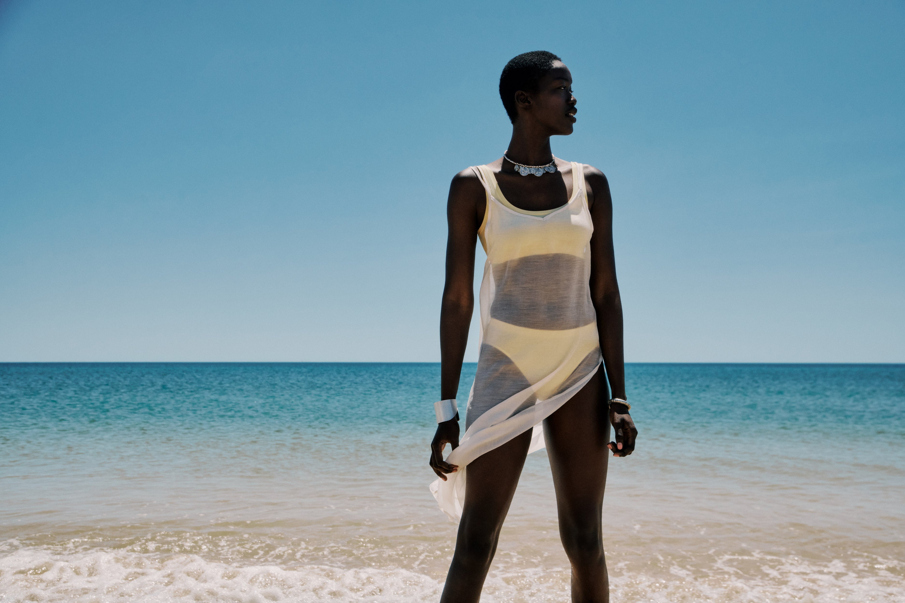 Woman in a Touch Feeling Crop Top and Briefs standing on a beach with clear blue water and sky.