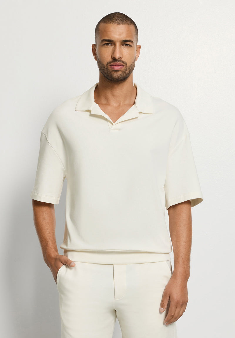 Man wearing a cream-colored polo shirt and pants against a light gray background