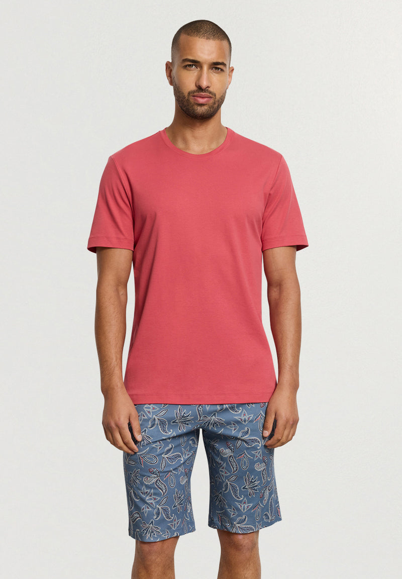 Man wearing a red t-shirt and blue patterned shorts on a white background