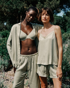 Two women wearing matching light green outfits standing outdoors with trees and lavender in the background.