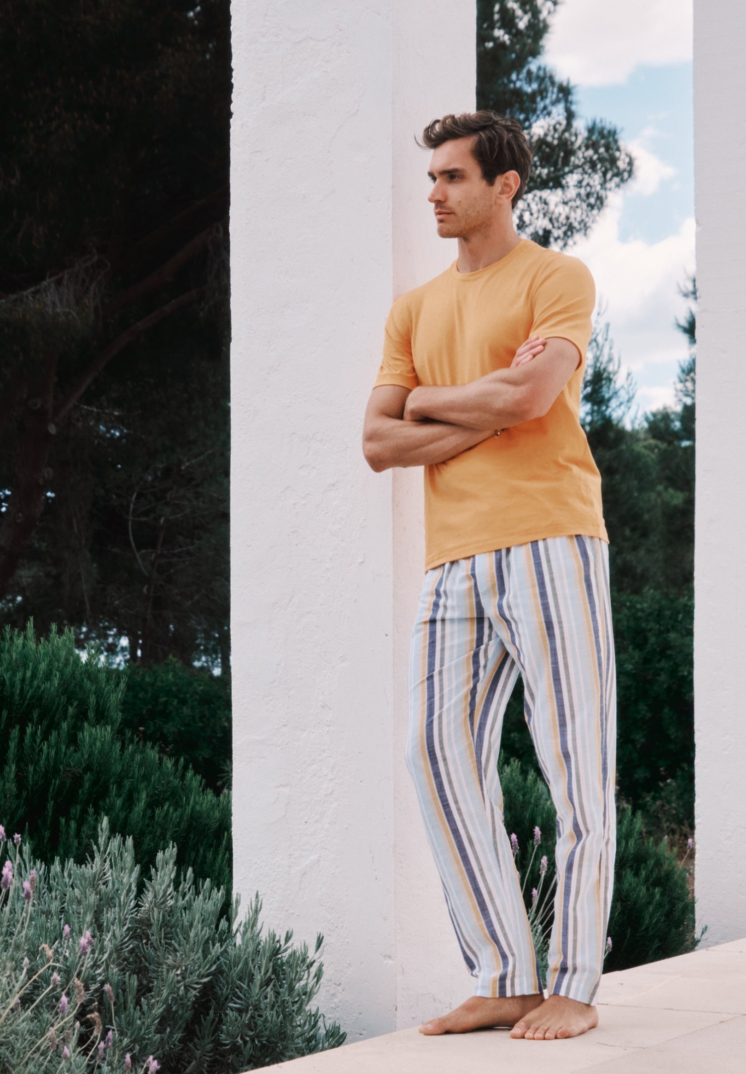 Man wearing a yellow shirt and striped pants standing outdoors with trees and sky in the background